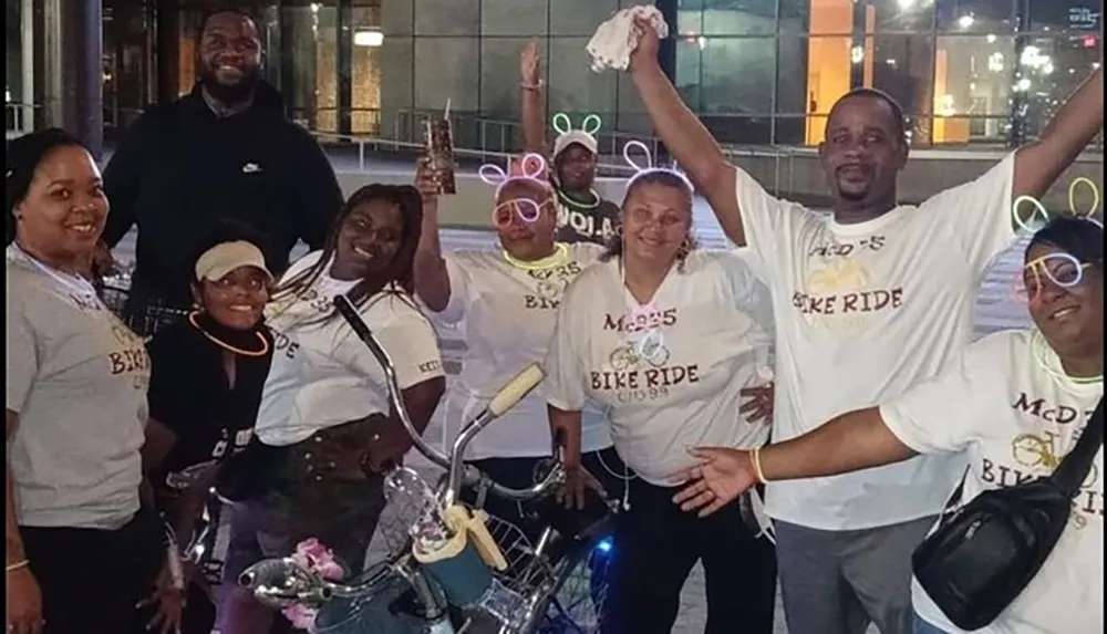 A group of joyful people in matching t-shirts are posing together at night likely at or after a bike ride event