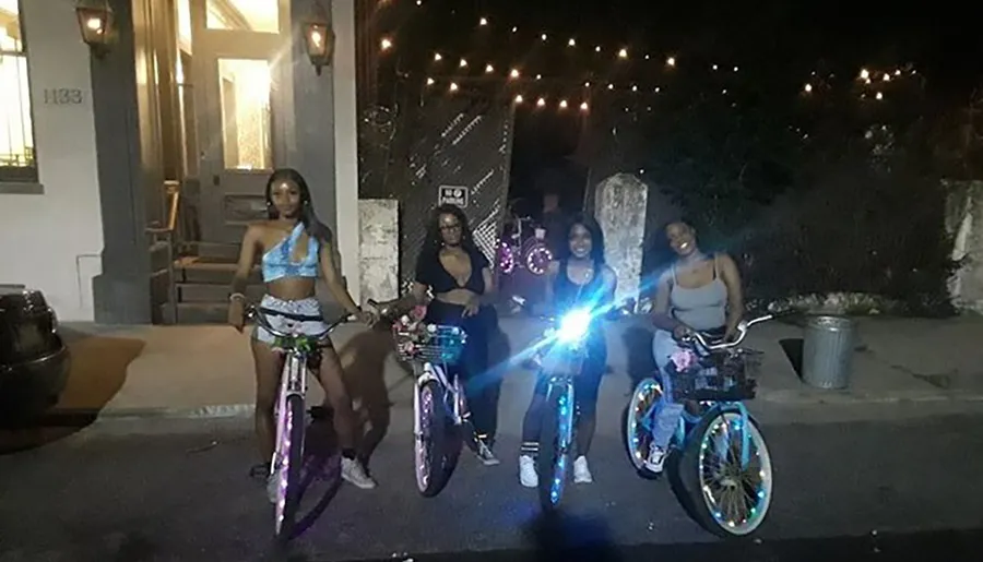 A group of people pose for a photo at night with their bicycles, which have bright, colorful lights on the wheels.