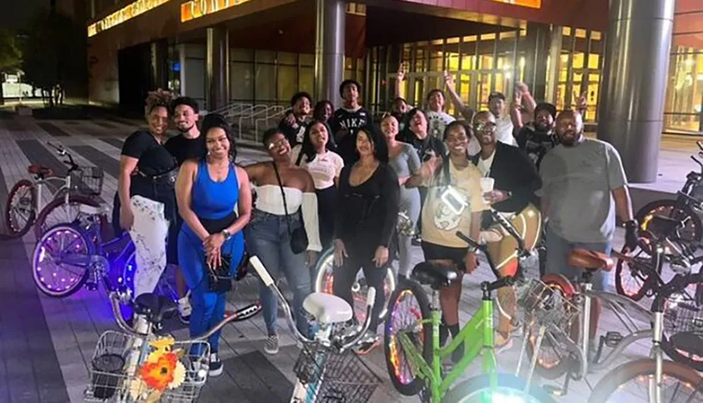 A group of smiling people some posing with bicycles appear to be enjoying a night out together