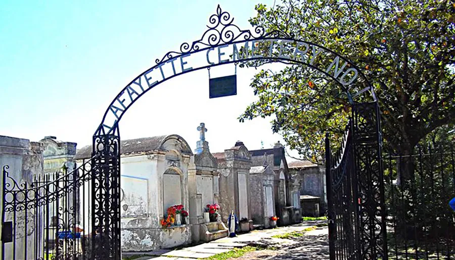 The image shows an ornate metal archway entrance labeled LAFAYETTE CEMETERY NO.1, leading to a historic cemetery with above-ground tombs and lush greenery.