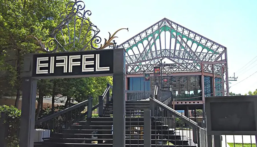 The image shows a metal archway labeled EIFFEL leading to a structure resembling an incomplete or stylized representation of the Eiffel Tower.