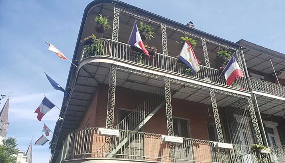 A two-story building with a wrought-iron balcony adorned with various flags and hanging plants under a clear blue sky