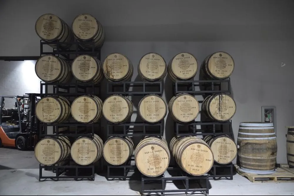 The image shows a storage area with several rows of wooden barrels likely containing wine or spirits stacked on metal racks