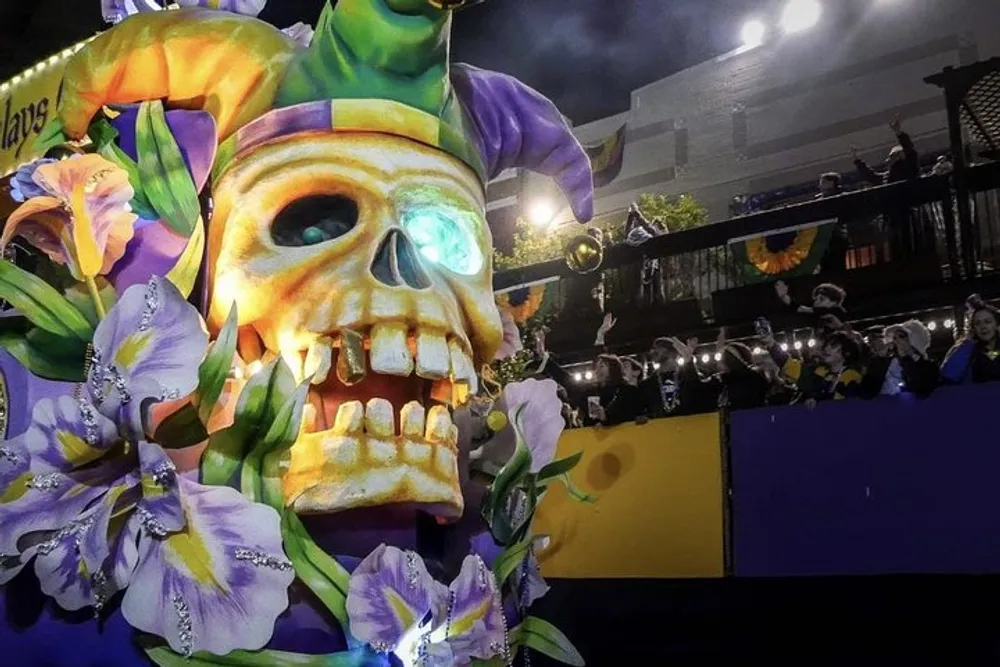 The image shows a vibrant Mardi Gras parade float featuring a large skull adorned with a jester hat and iris flowers with revelers in the background tossing beads to the crowd