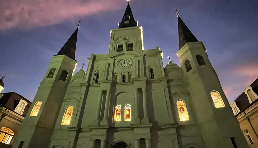 A historic church is illuminated against a twilight sky showcasing its stained glass windows and dual spires