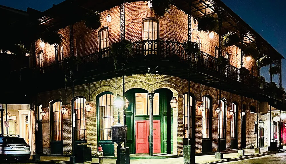 The image features a charming brick-built corner building at night illuminated by street lamps and adorned with wrought iron balconies and vibrant green shutters