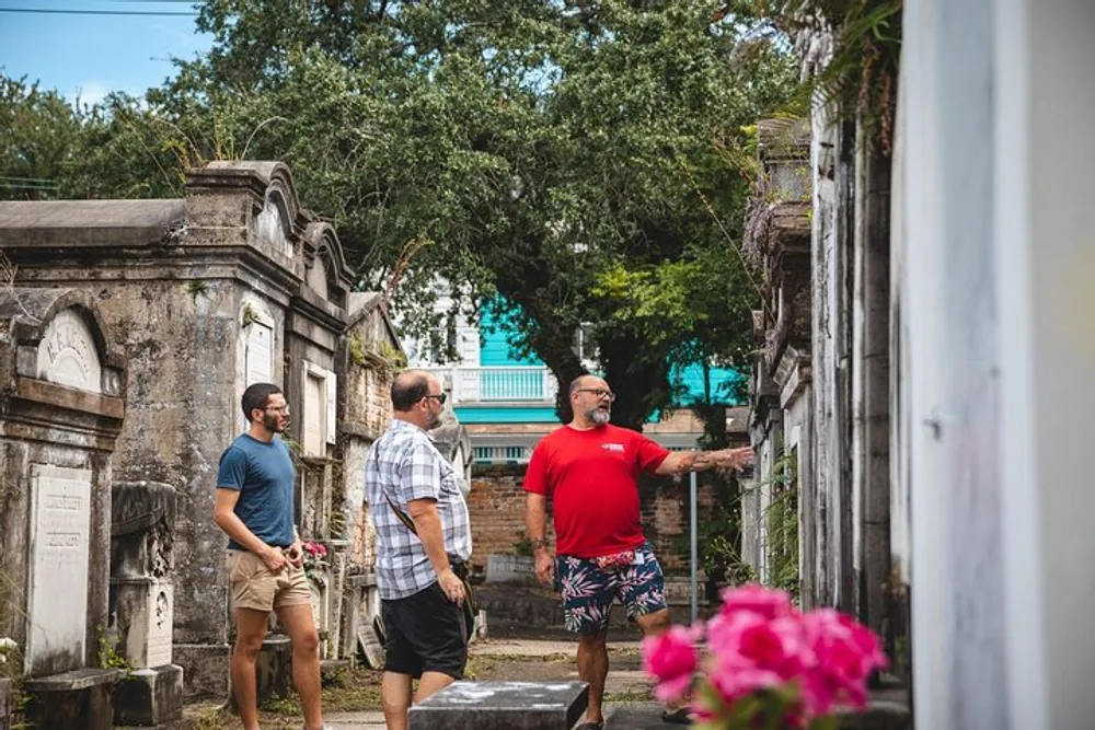 Three men are walking among old grave markers and crypts one of whom appears to be gesturing and explaining something to the others