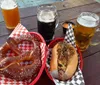 The image shows a casual outdoor dining setting featuring a large pretzel a loaded hot dog and three different beers on a wooden table