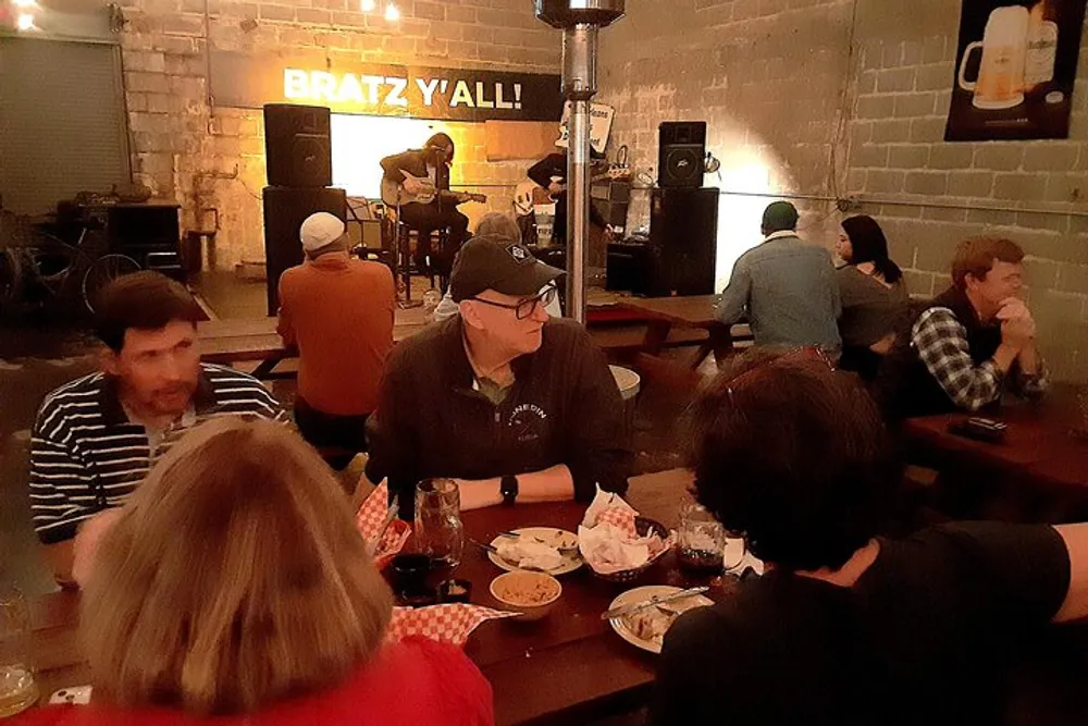People are dining and socializing at a casual indoor venue where a live musician is performing in the background