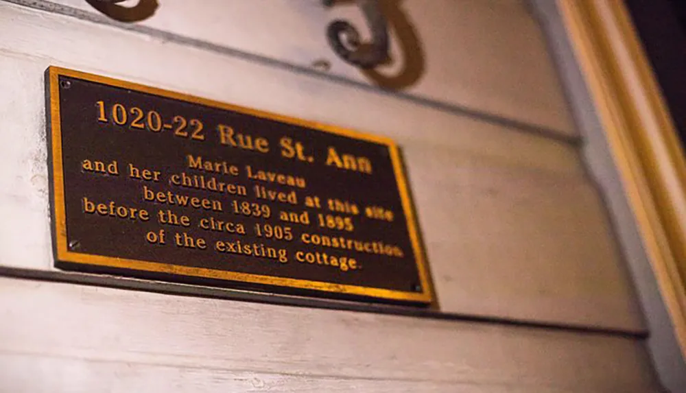 This image shows a commemorative plaque indicating that Marie Laveau and her children lived at the address 1020-22 Rue St Ann between 1839 and 1895 before the construction of the existing cottage circa 1905