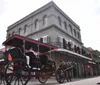 A horse pulling a red carriage with passengers on a sunny day through a street that hints at a New Orleans-style architecture