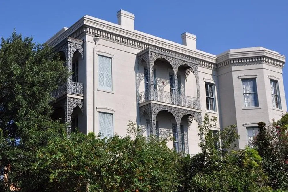 The image shows a two-story stucco building with ornate wrought iron balconies under a clear blue sky