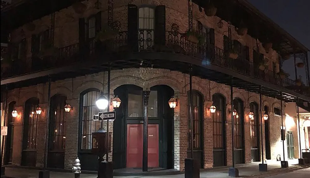 A two-story brick building with balconies and hanging plants illuminated by street lamps at night exudes historic charm