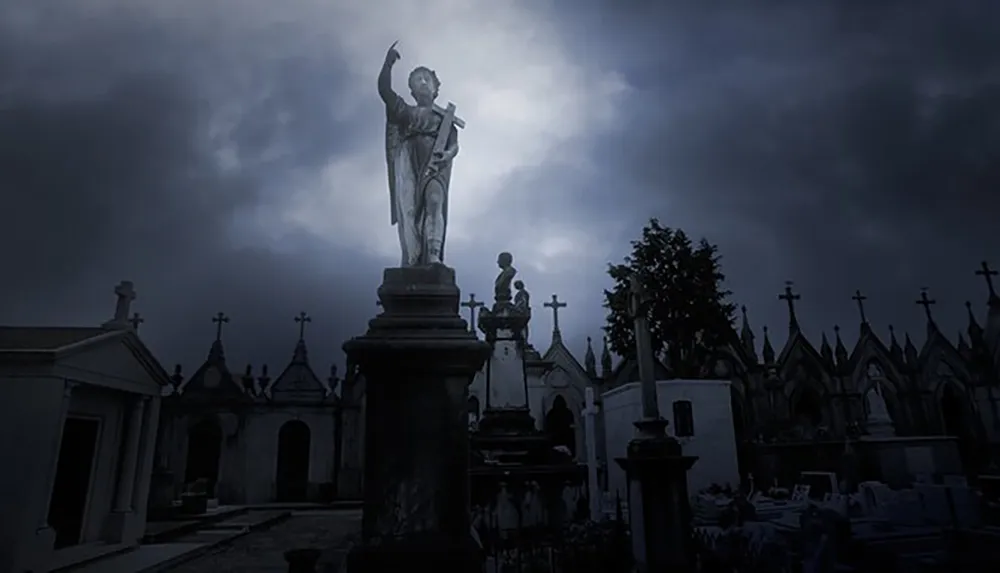 An angel statue towering over a cemetery is silhouetted against a brooding dark blue sky creating a somber and atmospheric scene