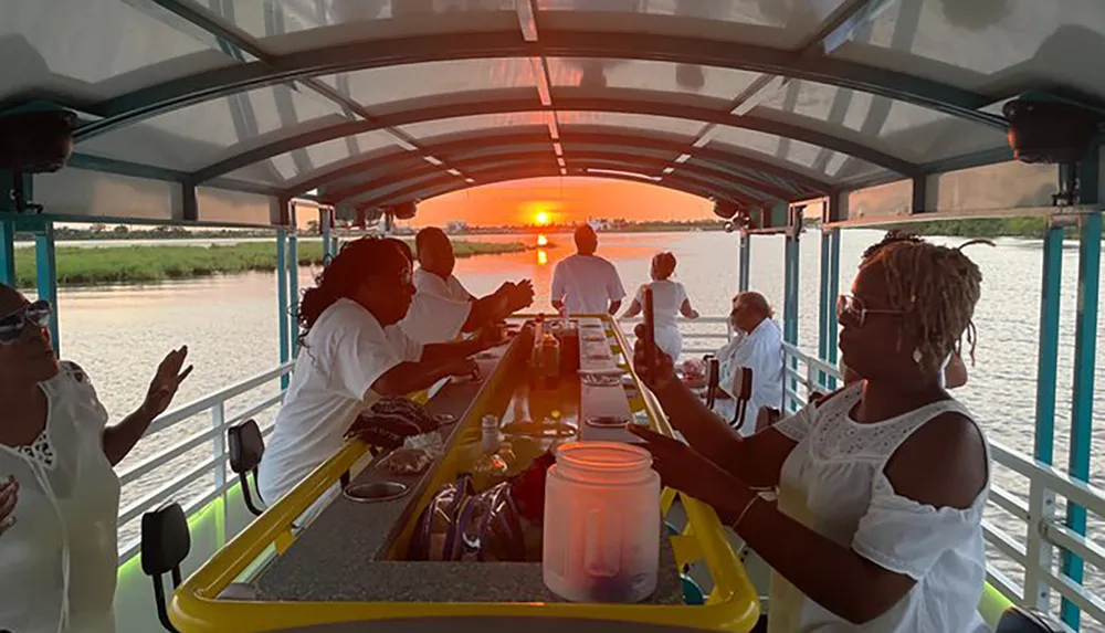 People are enjoying a meal on a boat with a beautiful sunset in the background