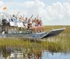 A group of people are enjoying a ride on an airboat through a grassy wetland area waving cheerfully