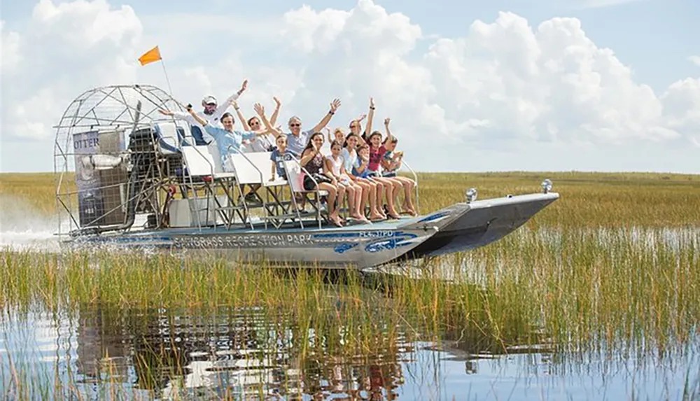 A group of people are enjoying a ride on an airboat through a grassy wetland area waving cheerfully