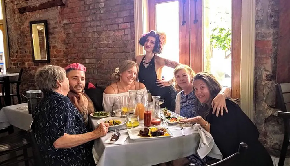 A group of people appears to be enjoying a lively meal together at a table in a restaurant with rustic brick walls and natural light coming from the windows