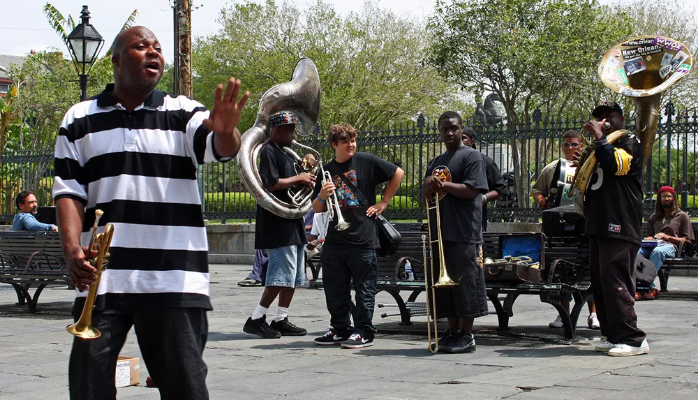 A group of musicians performs outdoors likely in a public space with various brass instruments and an enthusiastic front man singing or speaking to an audience