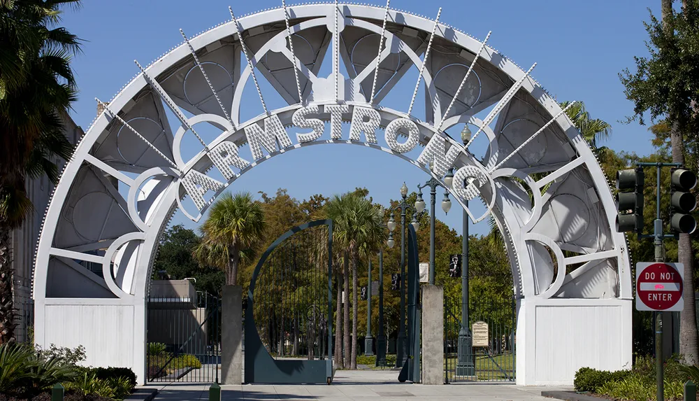The image features an elaborate white entrance gate with the word ARMSTRONG on it surrounded by palm trees under a blue sky