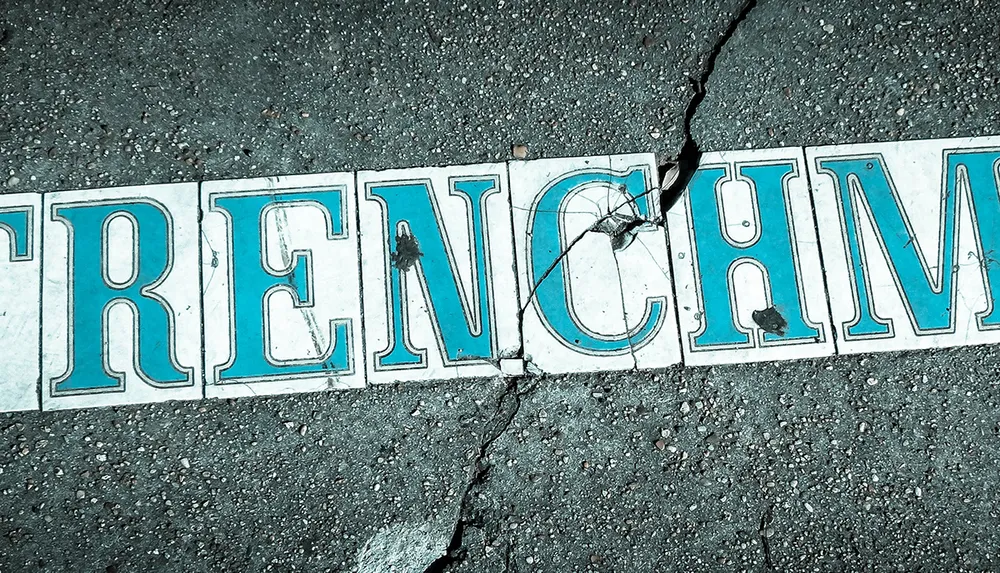 The image shows the word FRENCHM with a crack running through the letters on a textured ground surface