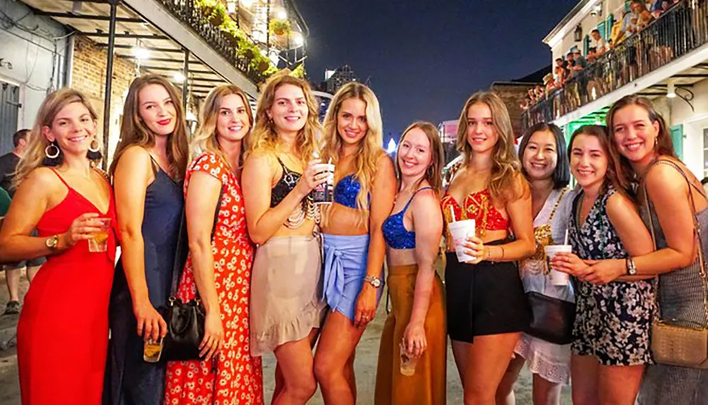 A group of smiling young women is posing for a photo at a lively outdoor evening venue