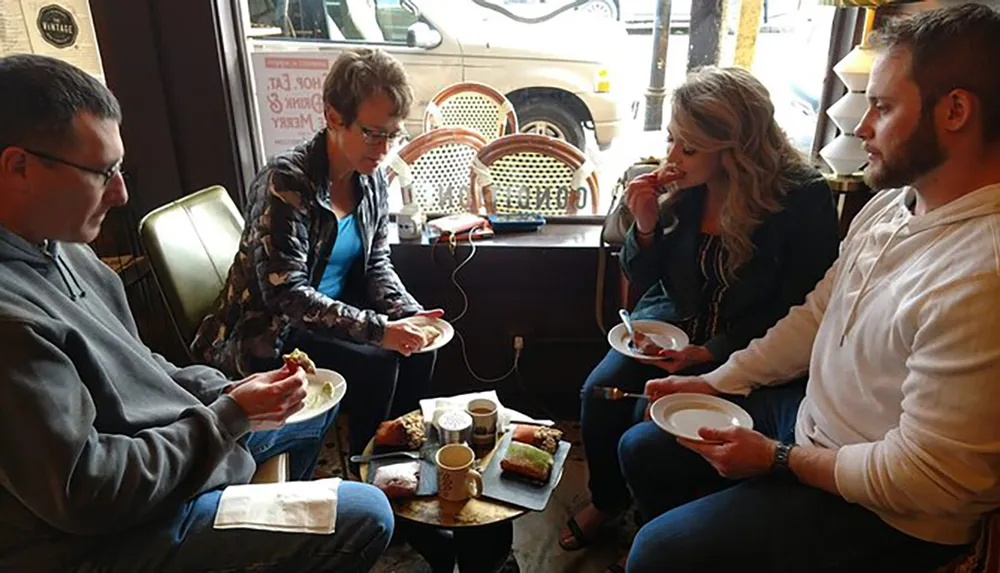 Four people are sitting in a cozy coffee shop setting enjoying beverages and pastries while engaged in conversation