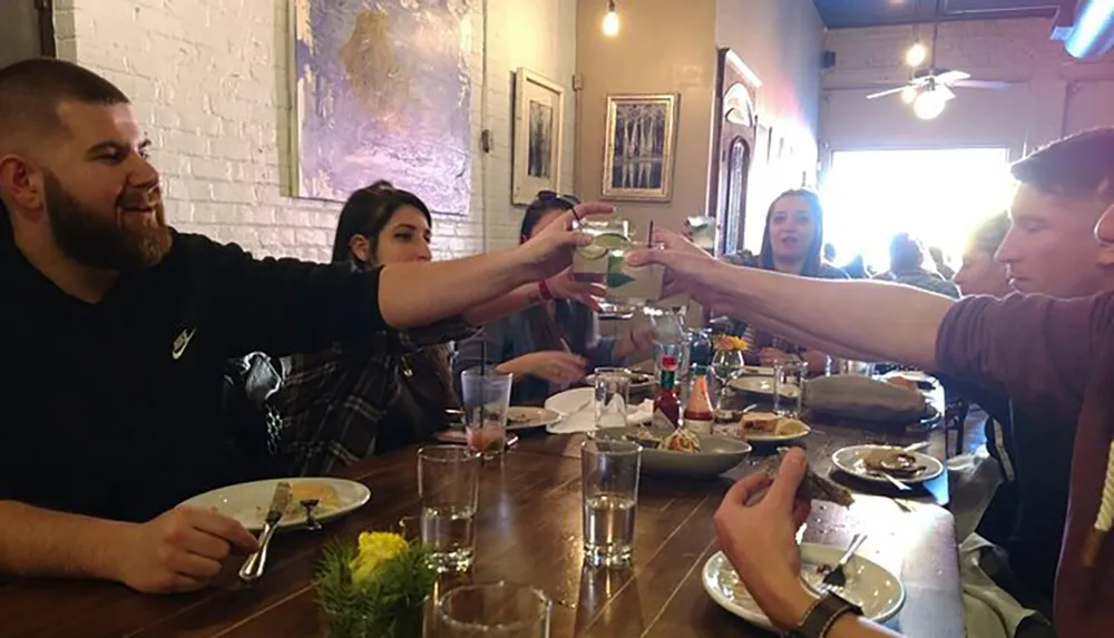 A group of friends are toasting drinks at a dining table in a restaurant setting