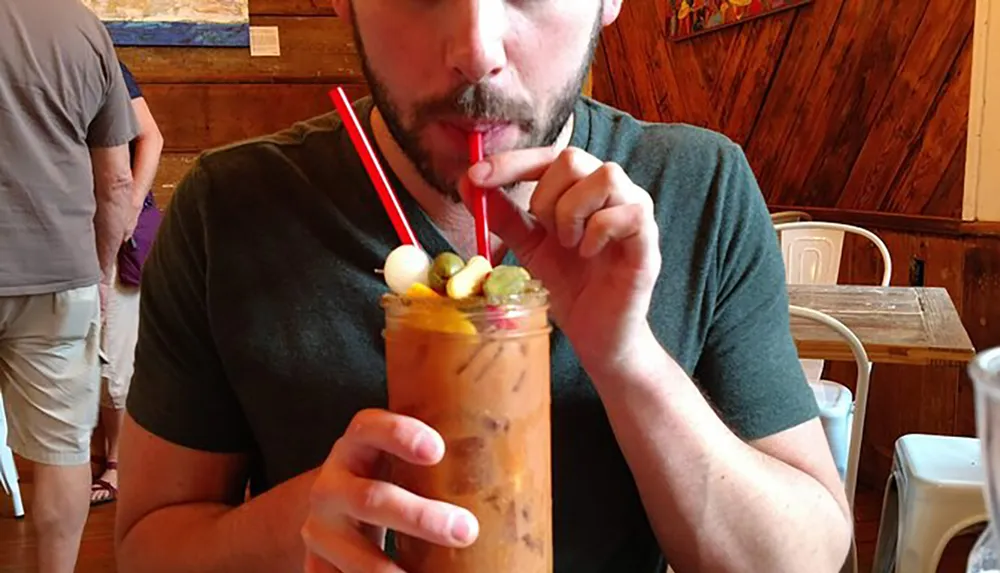 A man is drinking a garnished iced beverage through a straw