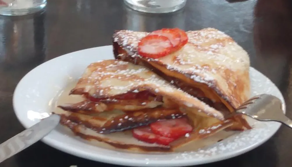 A plate of French toast dusted with powdered sugar and topped with strawberries appears ready to be enjoyed