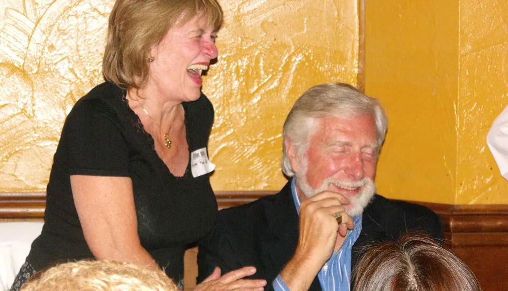 A man and a woman are seen sharing a hearty laugh together in a warmly lit room