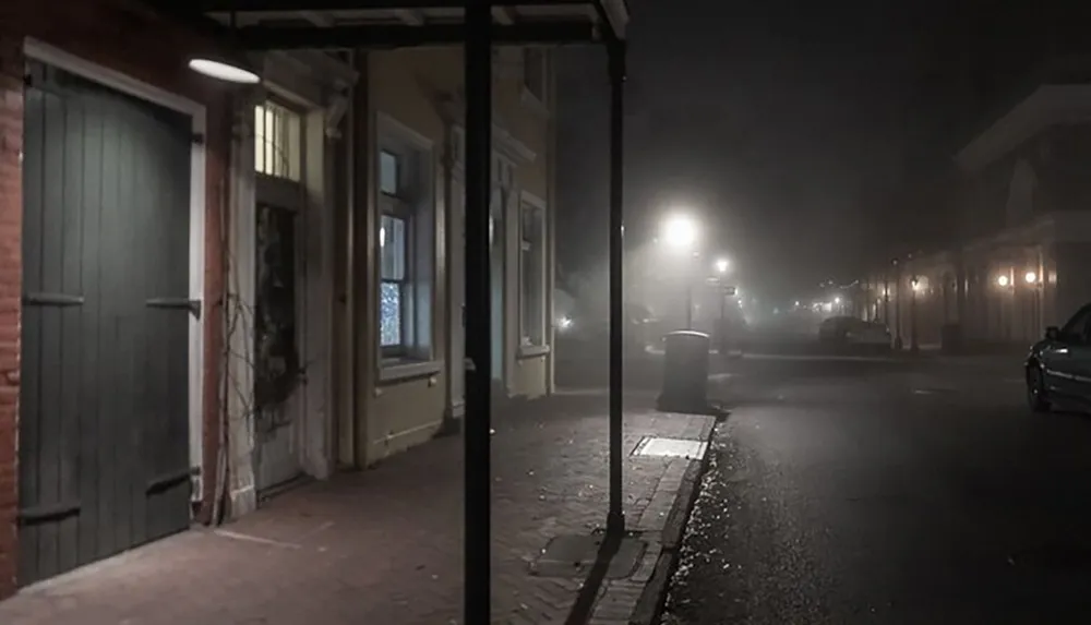 A foggy street at night with illuminated windows and street lights casting a hazy glow over the scene