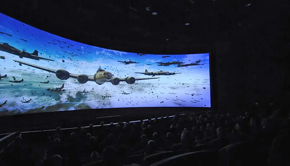 Audience members are watching an immersive space battle scene on a large curved movie theater screen