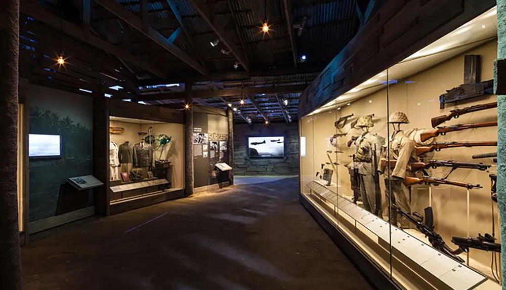 The image shows an exhibition space within a museum displaying military artifacts including uniforms and rifles under soft lighting