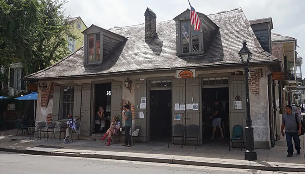 This image features a historical building with a weathered facade displaying the American flag and people casually gathered outside suggesting it is likely a place of interest or a business