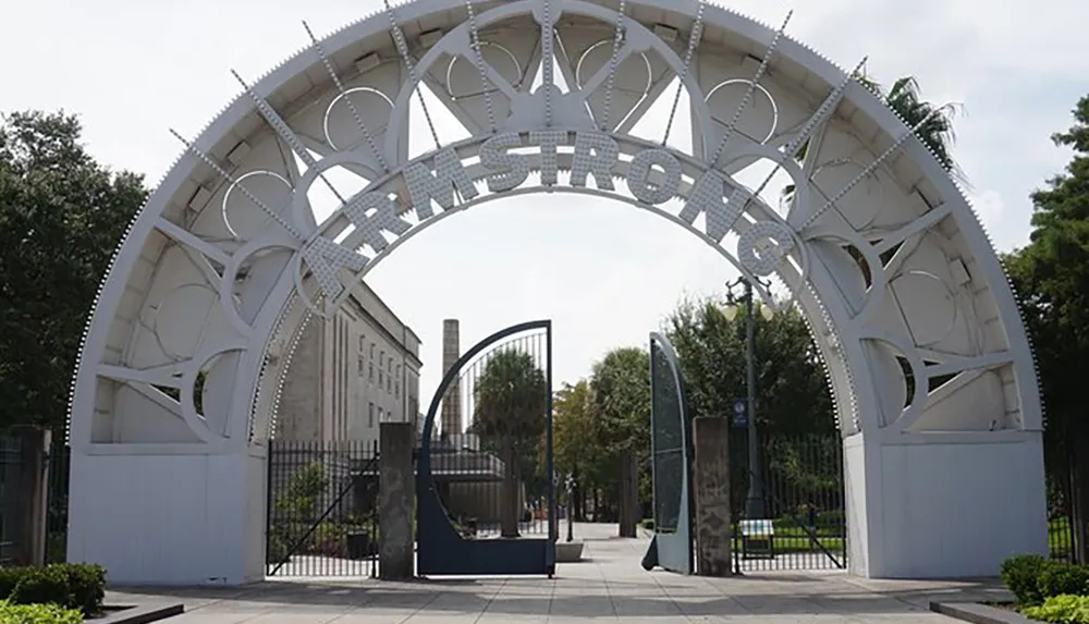The image shows an elaborate white gate with the word ARMSTRONG prominently displayed at the top set against a clear sky with some greenery in the background
