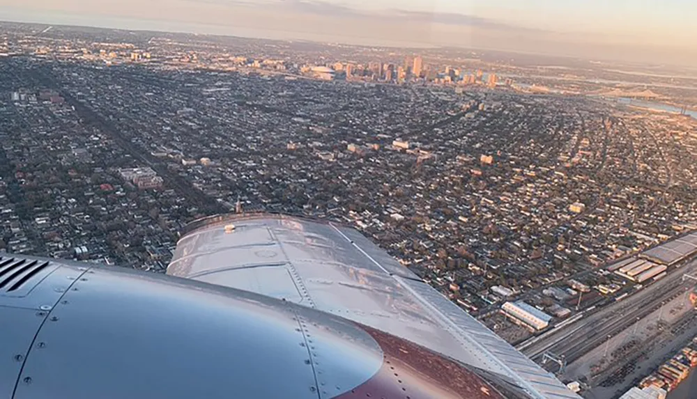 The image features a view from an airplane window showing part of the aircrafts wing and a sprawling cityscape below during what appears to be sunrise or sunset