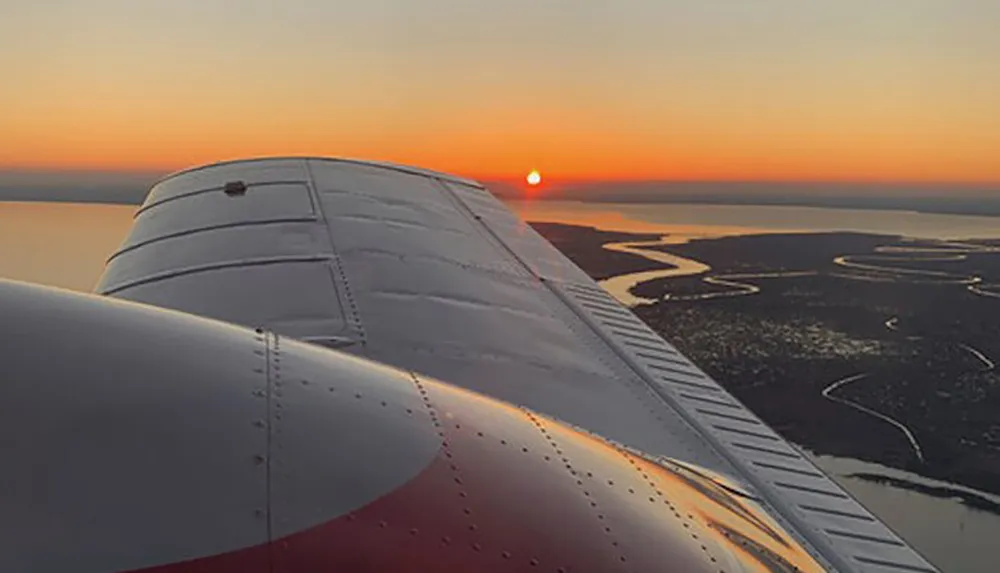The image captures a serene sunset view from the wing of an airplane in flight over a coastal landscape