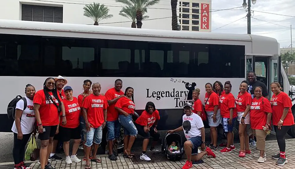 A group of people wearing matching red shirts pose for a photo in front of a Legendary Tours bus