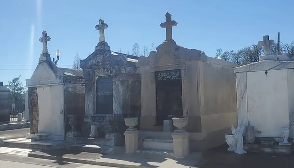 This image features a collection of above-ground tombs and mausoleums with ornate crosses on a sunny day characteristic of a historic cemetery often found in places with high water tables like New Orleans