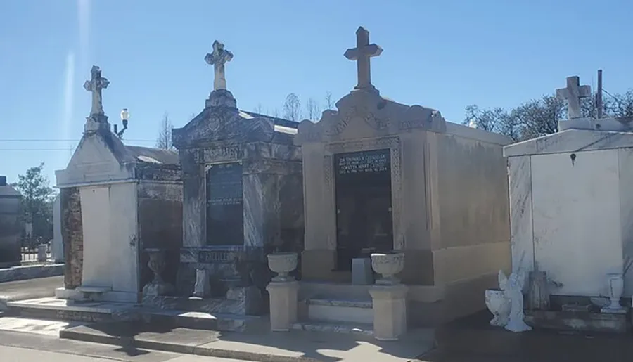 This image features a collection of above-ground tombs and mausoleums with ornate crosses on a sunny day, characteristic of a historic cemetery often found in places with high water tables, like New Orleans.
