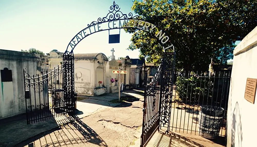 The image shows the ornate entrance gate to Lafayette Cemetery No 1 surrounded by aged crypts under a clear sky