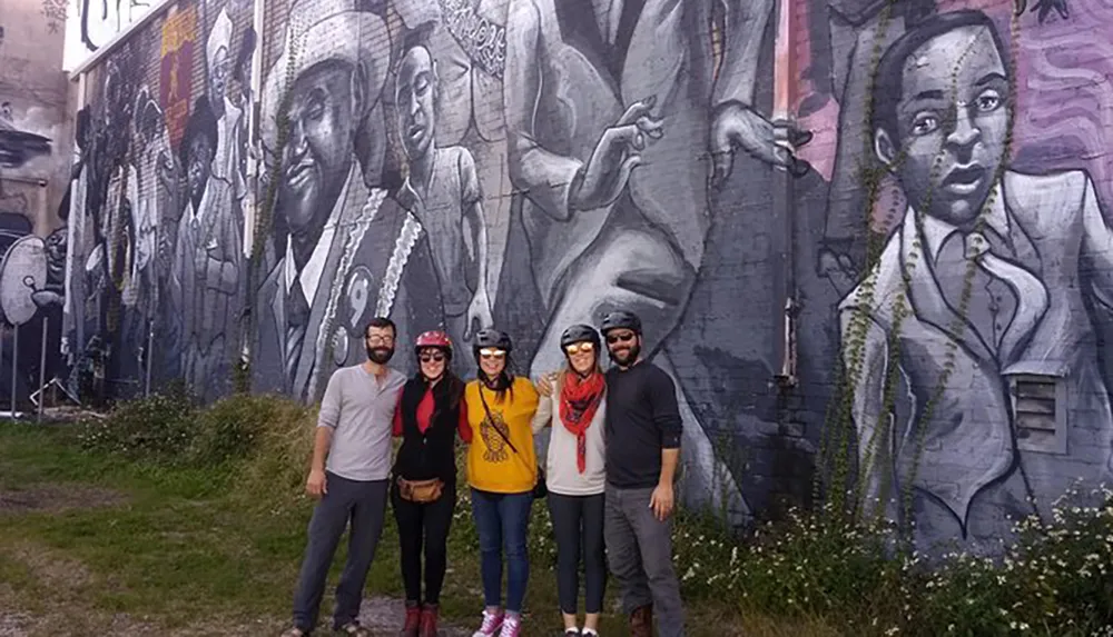 Four people wearing helmets are posing in front of a large monochromatic mural featuring jazz musicians