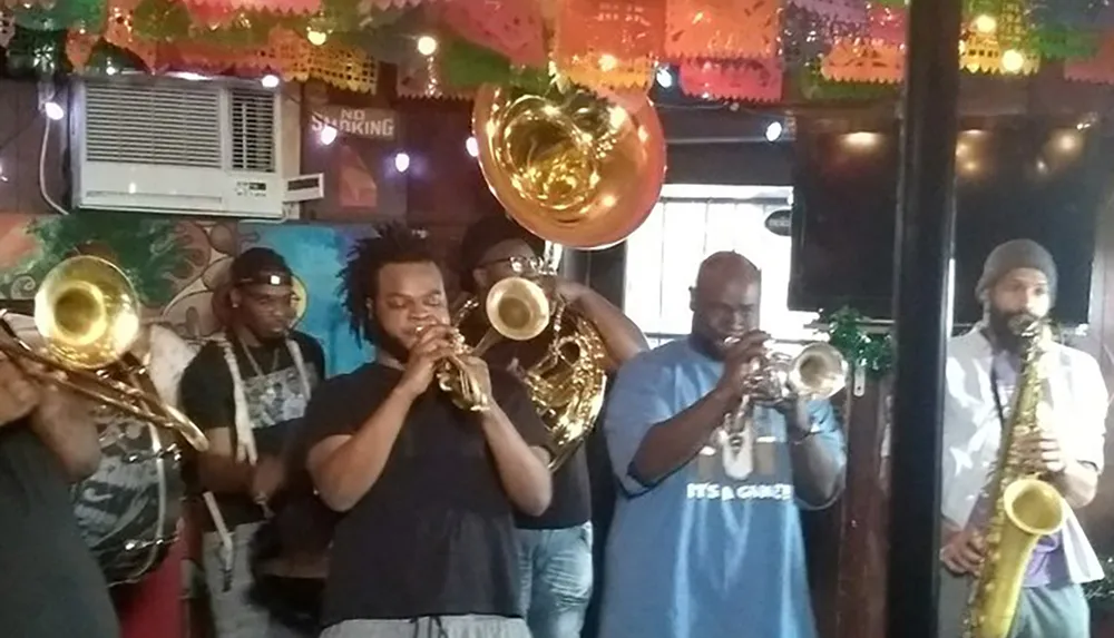 A group of musicians is performing with brass instruments in a lively indoor setting adorned with colorful decorations