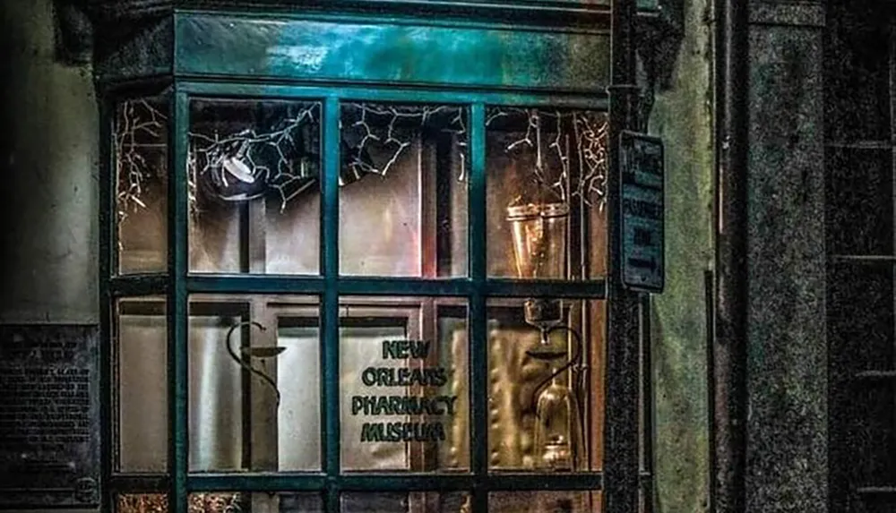 The image shows a dimly lit eerie storefront of the New Orleans Pharmacy Museum with cracked window panes and vintage pharmacy equipment visible through the glass
