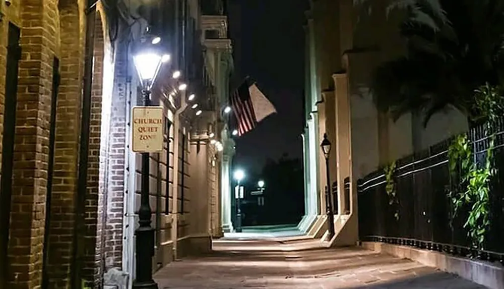 An illuminated narrow alleyway at night with a CHURCH QUIET ZONE sign and an American flag in the background