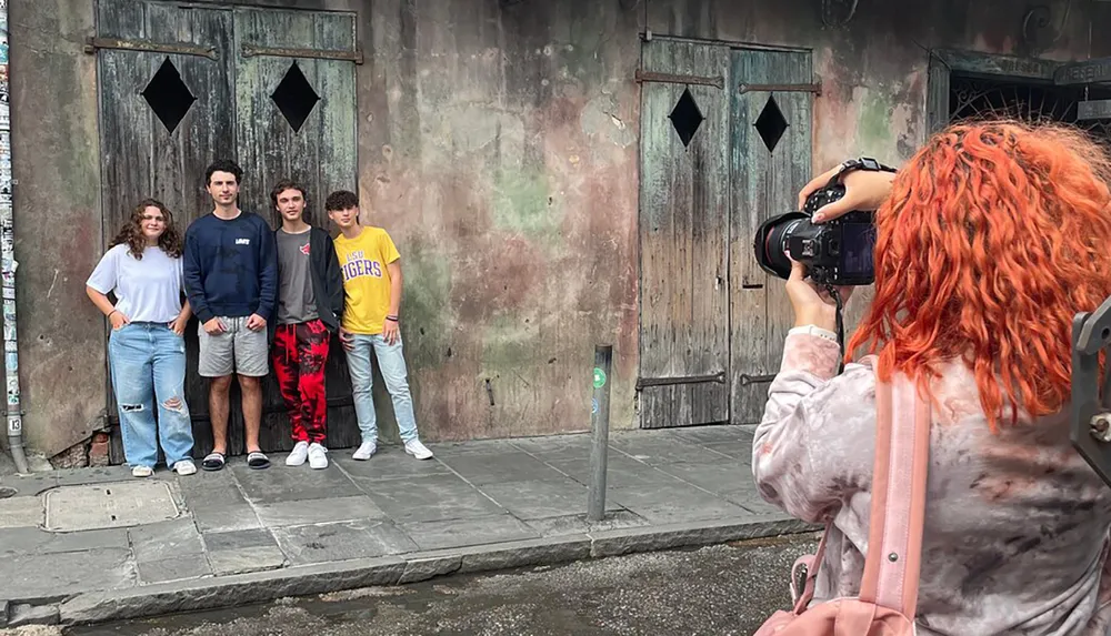A person with orange hair is taking a photo of four people posing in front of an old weathered door