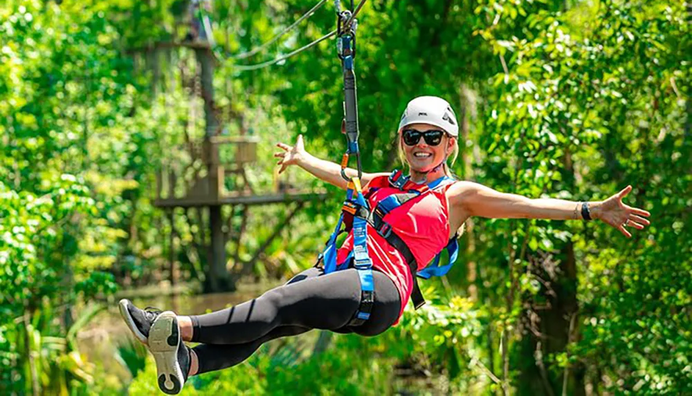 A person is smiling excitedly while zip-lining amidst lush greenery