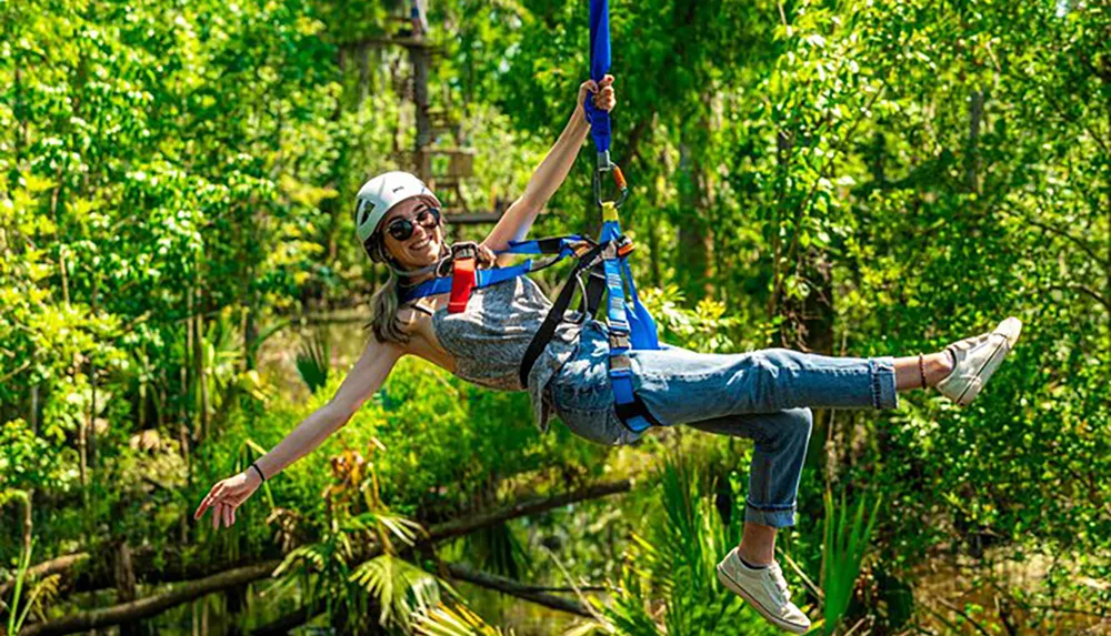 A person is gleefully zip-lining above a lush forest wearing a helmet and harness for safety