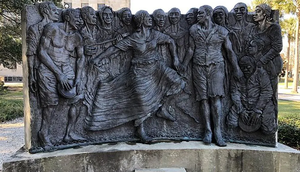 The image shows a bas-relief sculpture featuring a group of people portrayed in a dynamic and expressive manner likely commemorating a specific historical event or cultural narrative